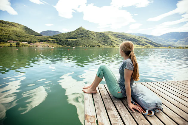 Una ragazza è seduta su un pontile al lago di Caldaro