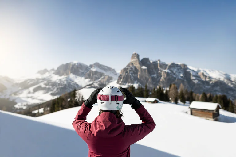 Una donna in tuta da sci si tira gli occhiali da sci sul viso mentre guarda le Dolomiti.
