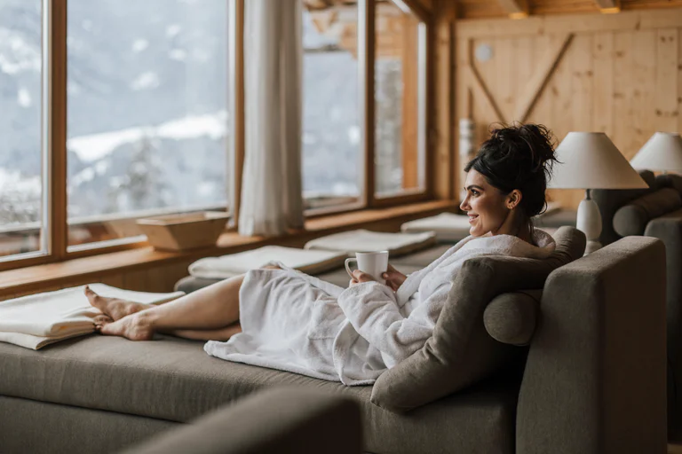A woman is lying in a bathrobe with a cup of tea on a lounger in the spa.