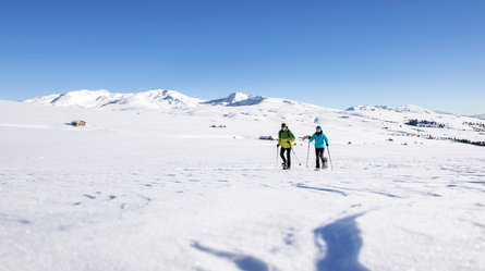 A man and a woman hiking with snow shoes over the snow-covered Villanderer Alm Alpine pasture