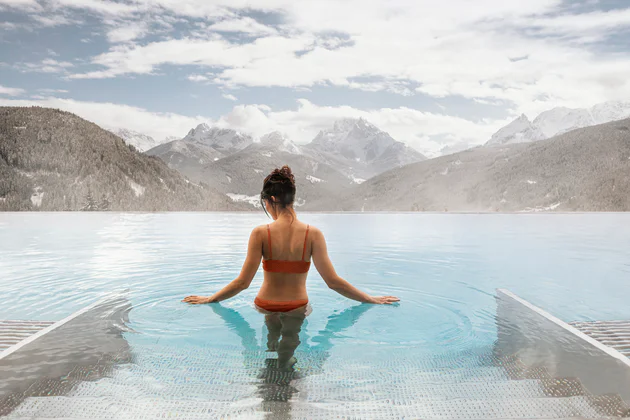 Woman standing up to her stomach in an outdoor thermal pool looking out over a mountain panorama.