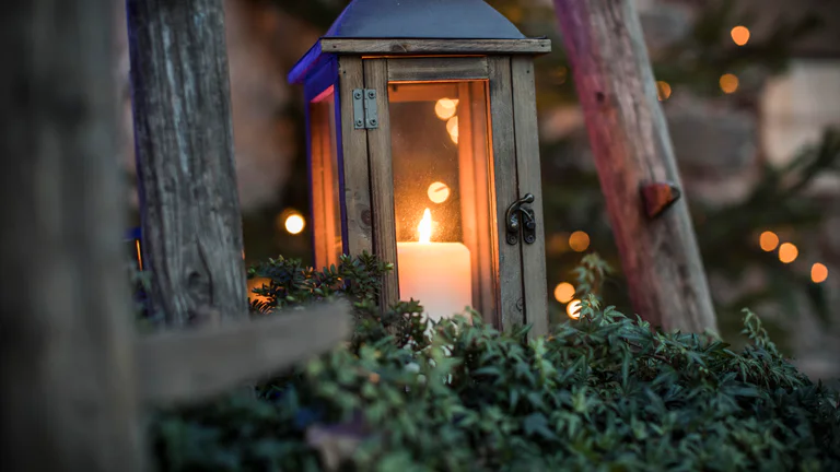 A lantern made of wood and glass with a glowing candle inside.