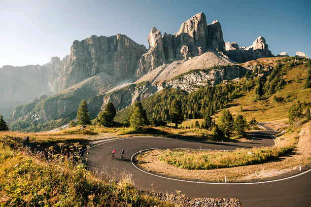 Zwei Rennradfahrer sind bei schönstem Wetter auf einer Serpentine in der Dolomitenregion Alta Badia unterwegs.