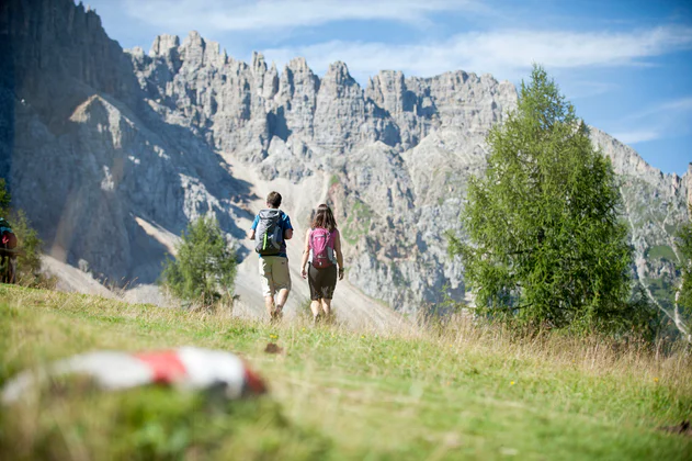 Una coppia di escursionisti in cammino tra parati e monti della Val D'Ega
