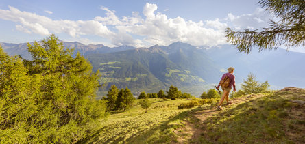 A person enjoys hiking in the mountains in the area of Schlanders & Laas/Silandro & Lasa during a sunny summer day