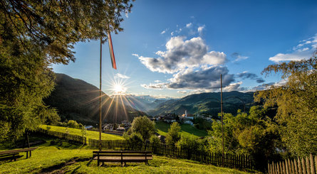 Vista sul verdeggiante paese di Collepietra con un panorama montuoso e un sole splendente sullo sfondo