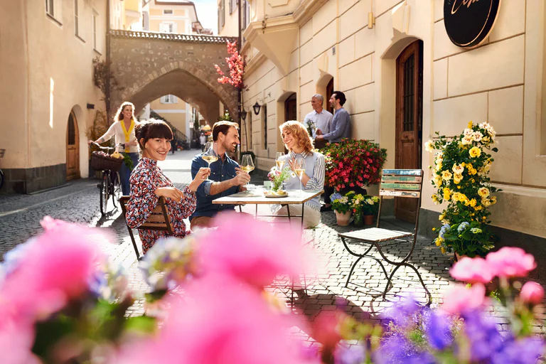Due donne e due uomini sorridono e si godono un aperitivo all'aperto nel centro storico di Bolzano.