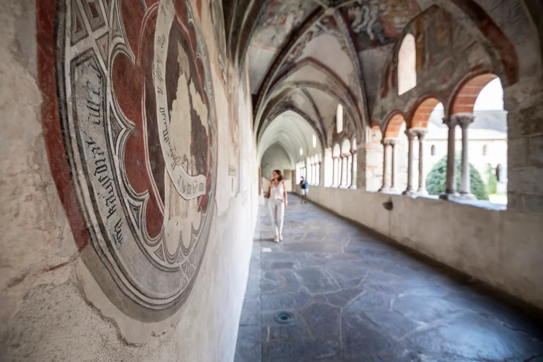 Una donna cammina lungo il chiostro del Duomo di Bressnone ammirando gli splendidi affreschi 