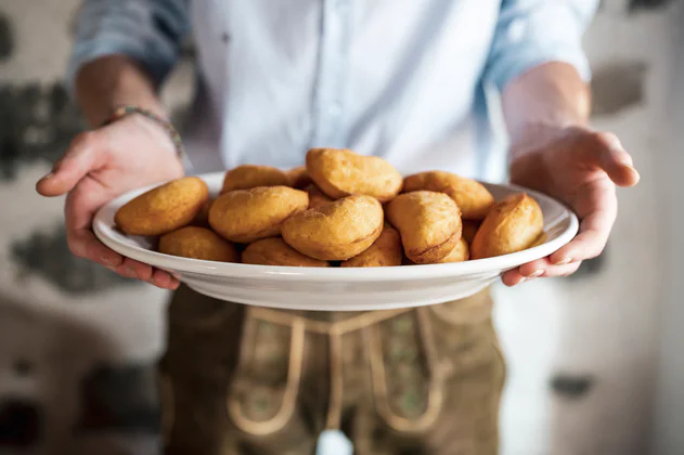 A man holds a plate full of Canci Checi, i.e., traditional Ladin deep-fried Schlutzkrapfen ravioli.