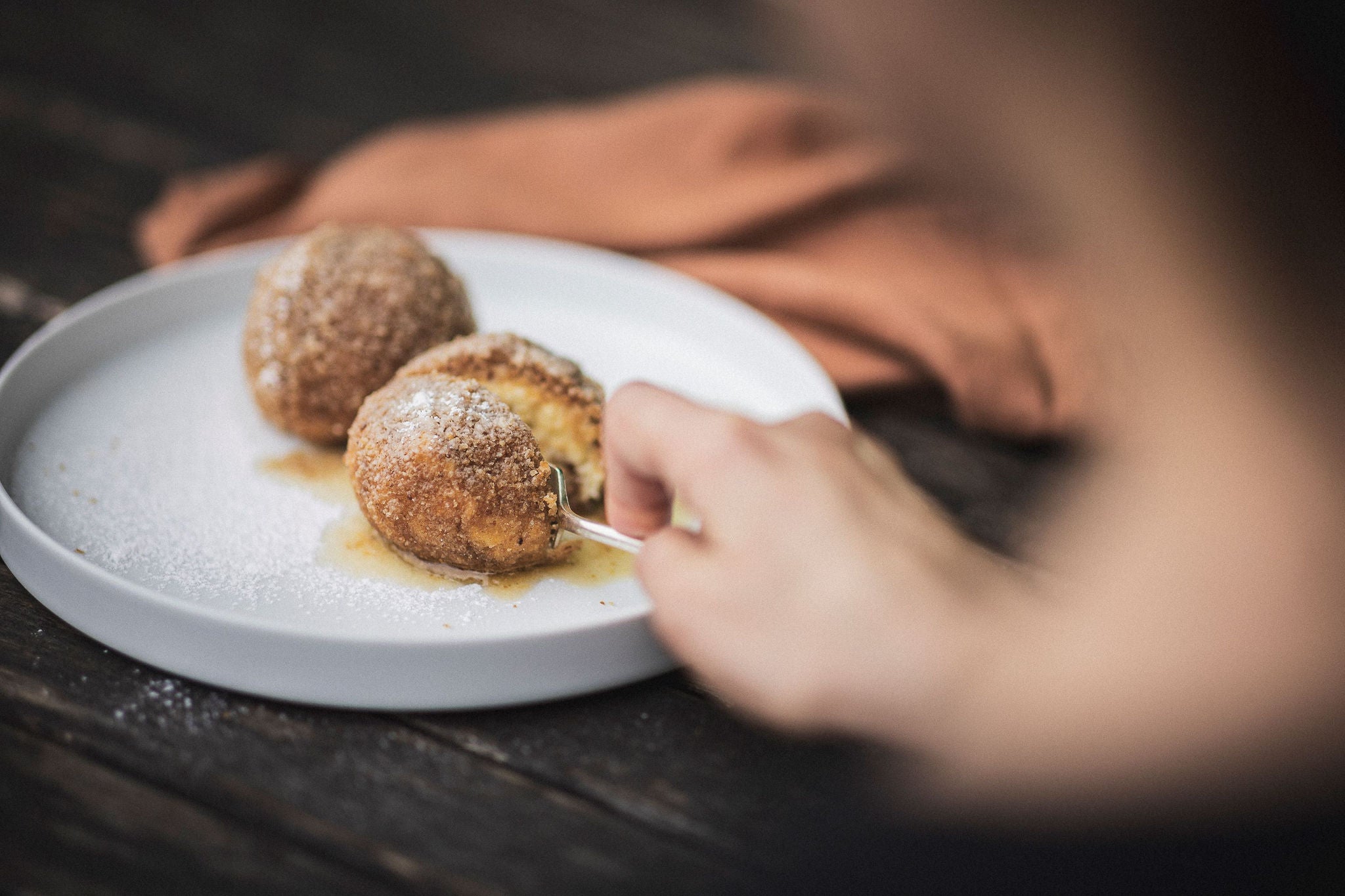 Eine Hand zerteilt mit der Gabel einen Marillenknödel.