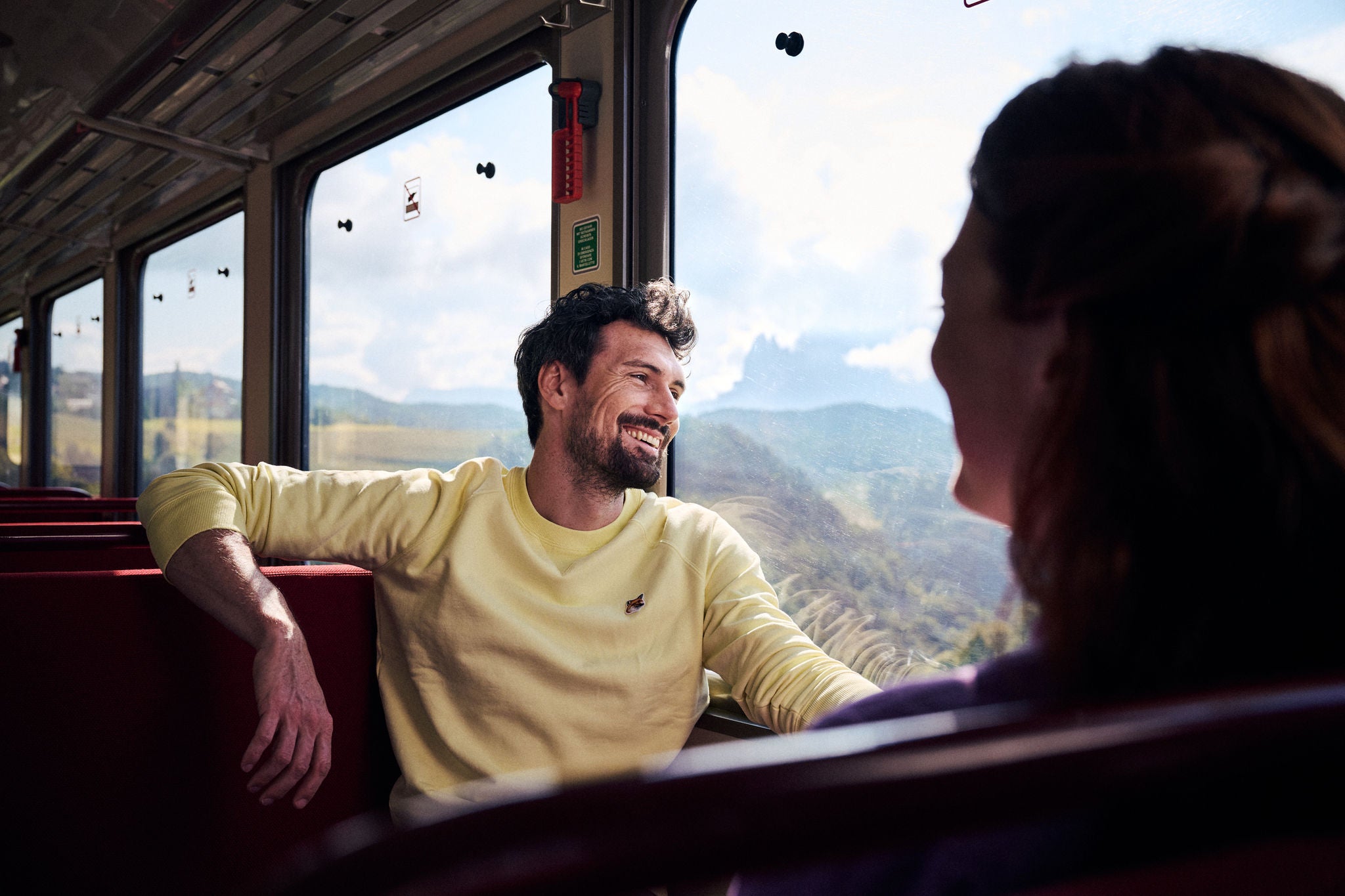 Ein junges Paar sitzt sich in einem Waggon der Rittner Bahn gegenüber, vor dem Fenster streift die Landschaft vorbei.