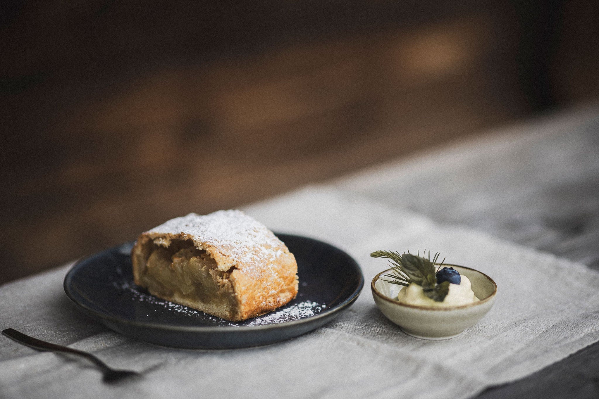 Ein Teller mit einem Stück Apfelstrudel und daneben ein Schälchen mit Schlagsahne.