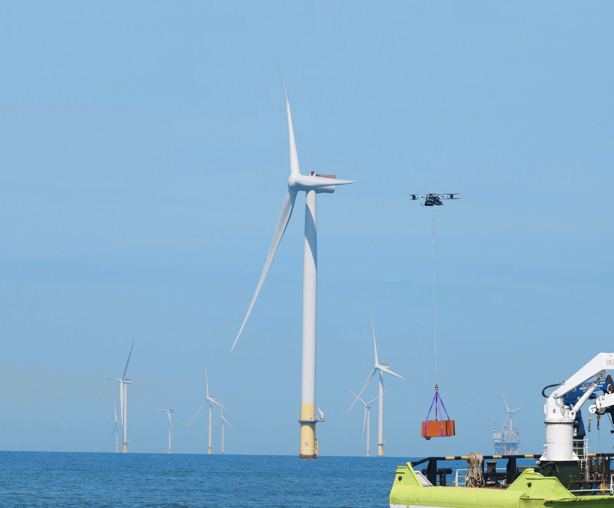 Eine Drohne transportiert einen Container über dem offenen Meer mit Windturbinen. im Hintergrund.