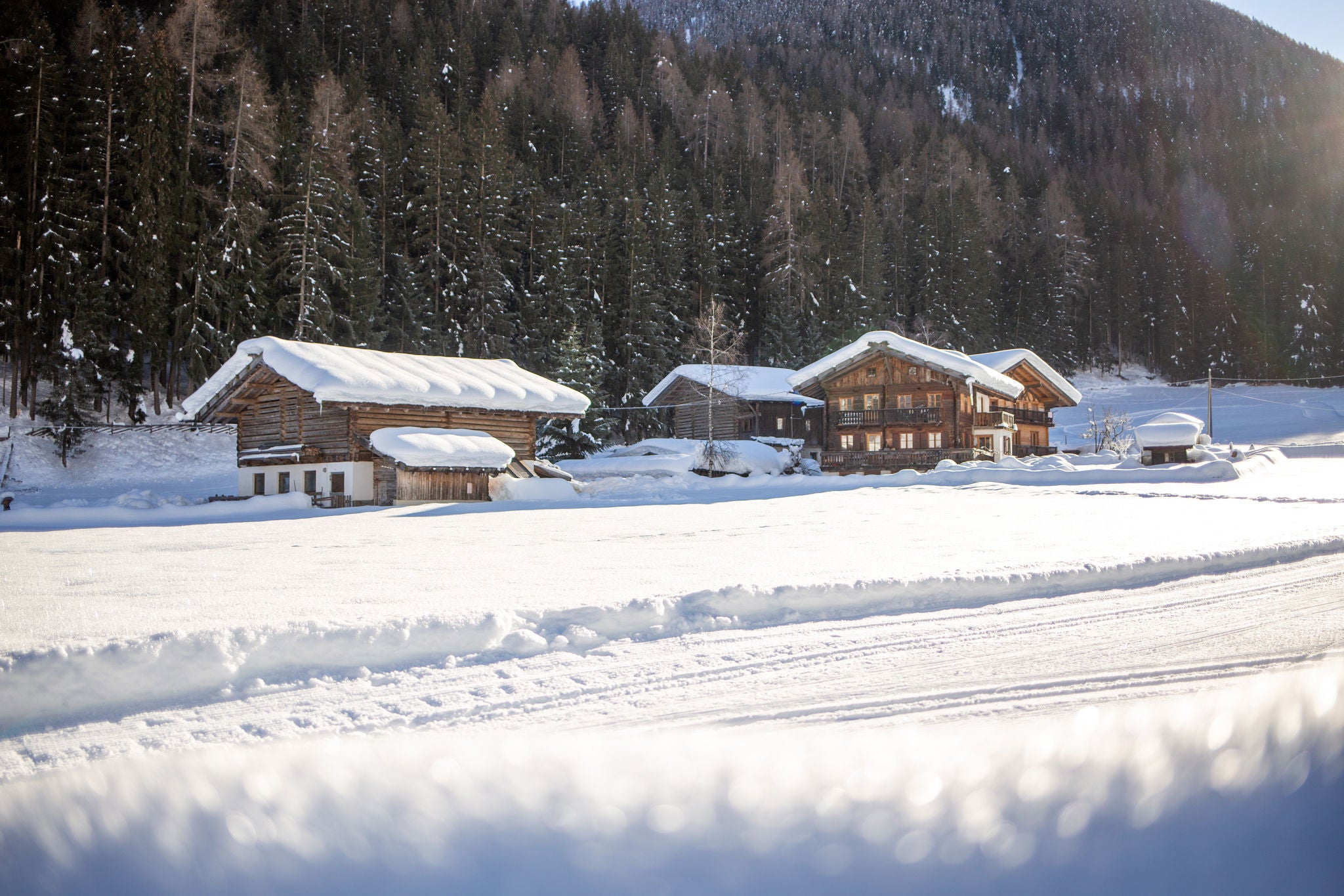 Langlaufloipe mit beschneiten Almhütten im Ultental