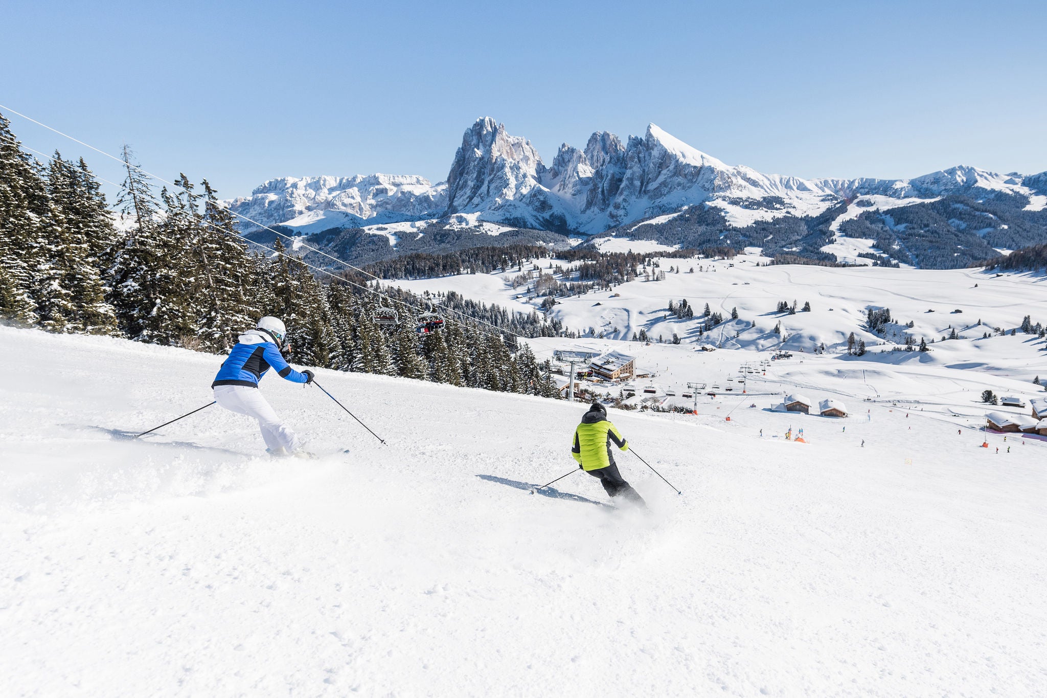 Zwei Skifahrer bei Abfahrt auf einer Skipiste auf der Seiser Alm mit Blick auf Plattkofel und Langkofel