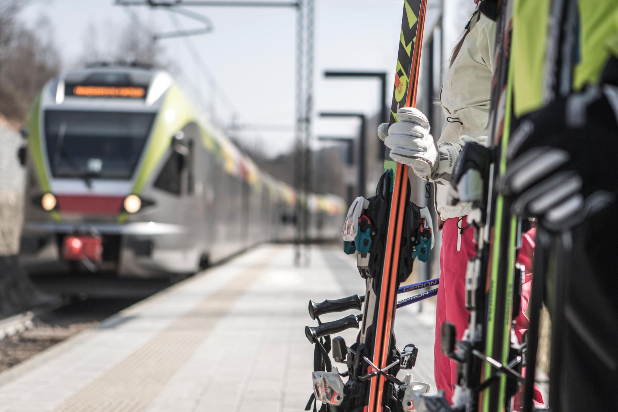 Skifahrer warten mit ihren Ski am Bahnsteig auf einen einfahrenden Regionalzug