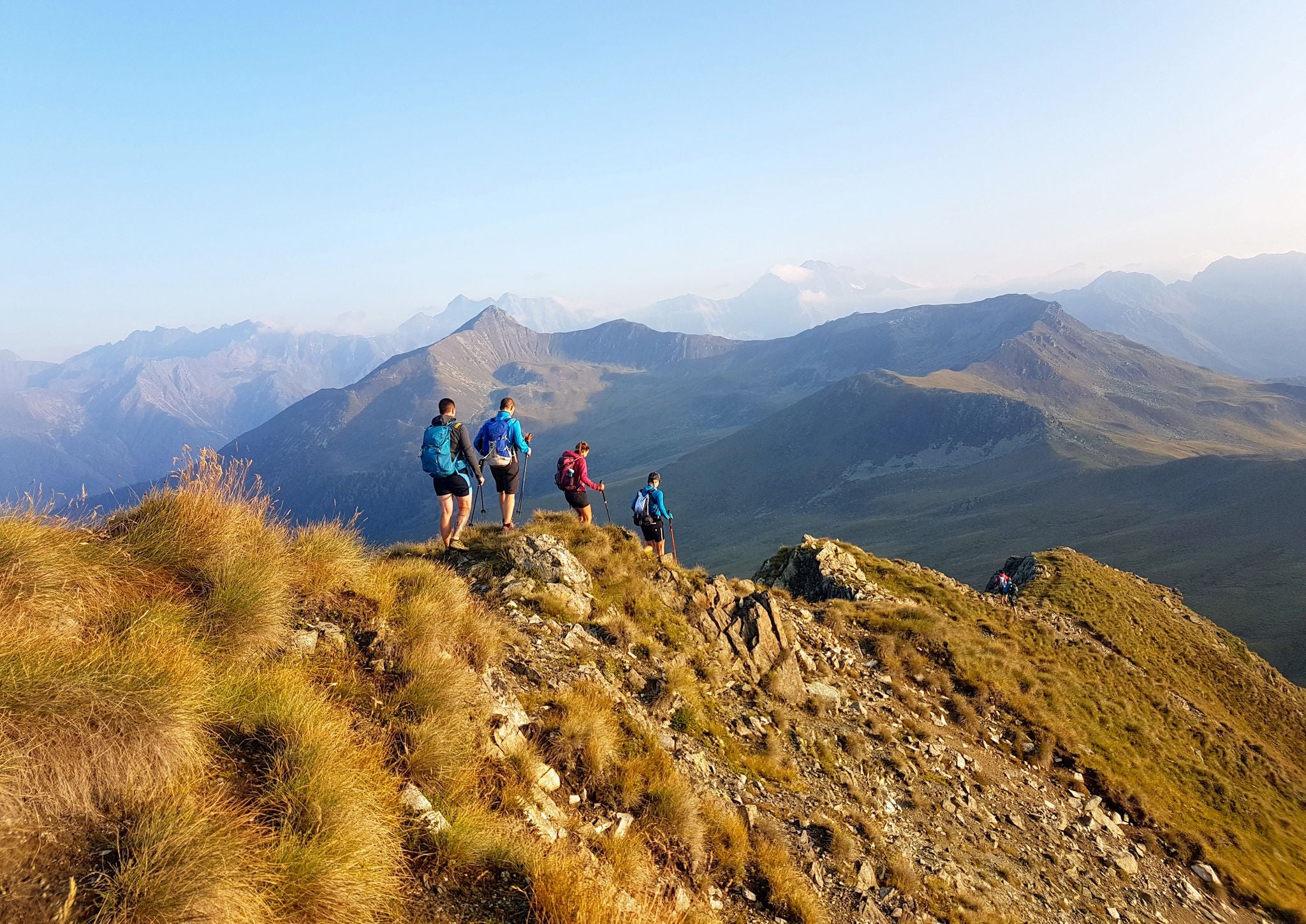 Vier Personen wandern auf einem Bergkamm nordwärts, am Horizont ein Band aus Gipfeln.