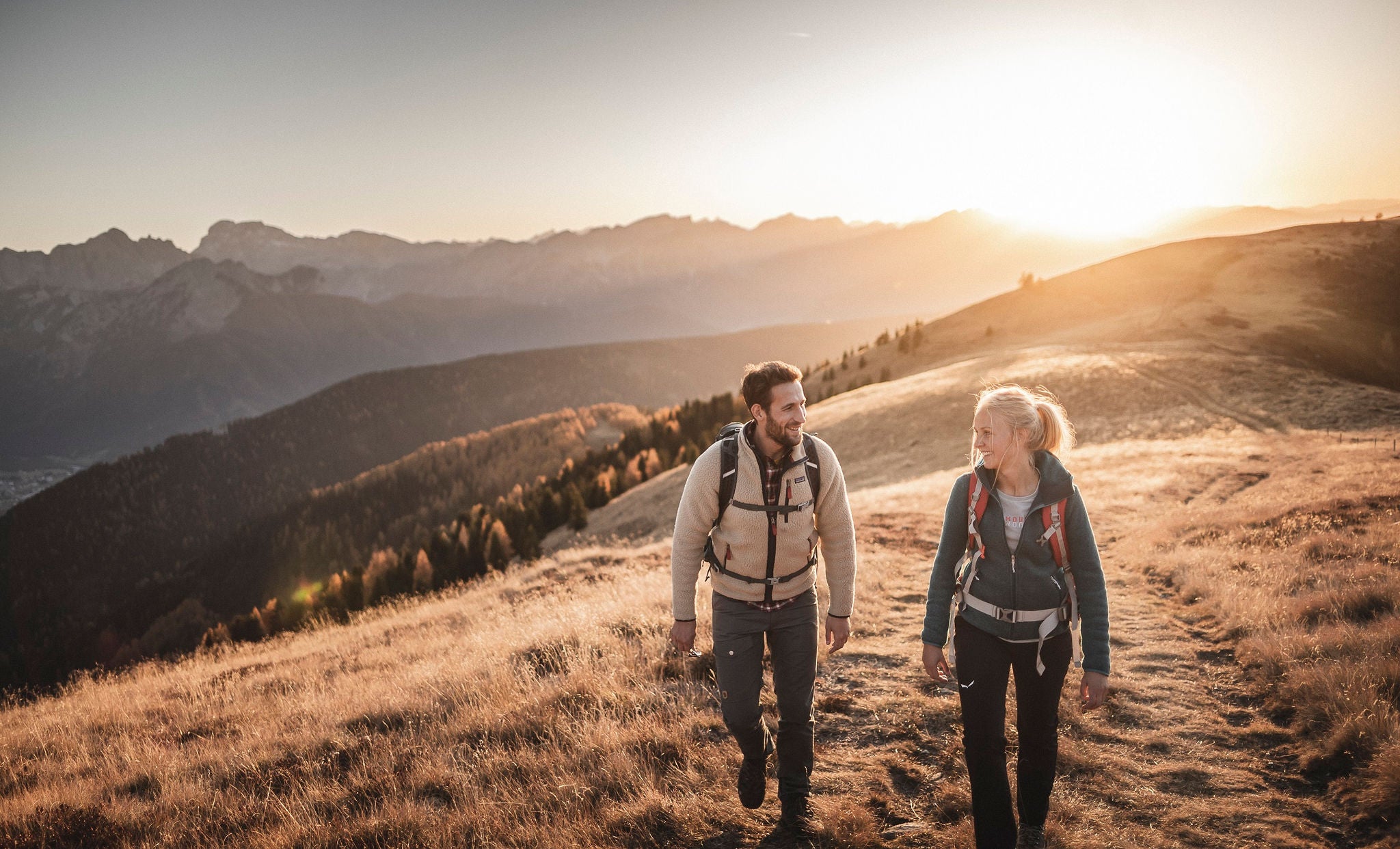 Ein Mann und eine Frau wandern im Herbstlicht über eine Almwiese