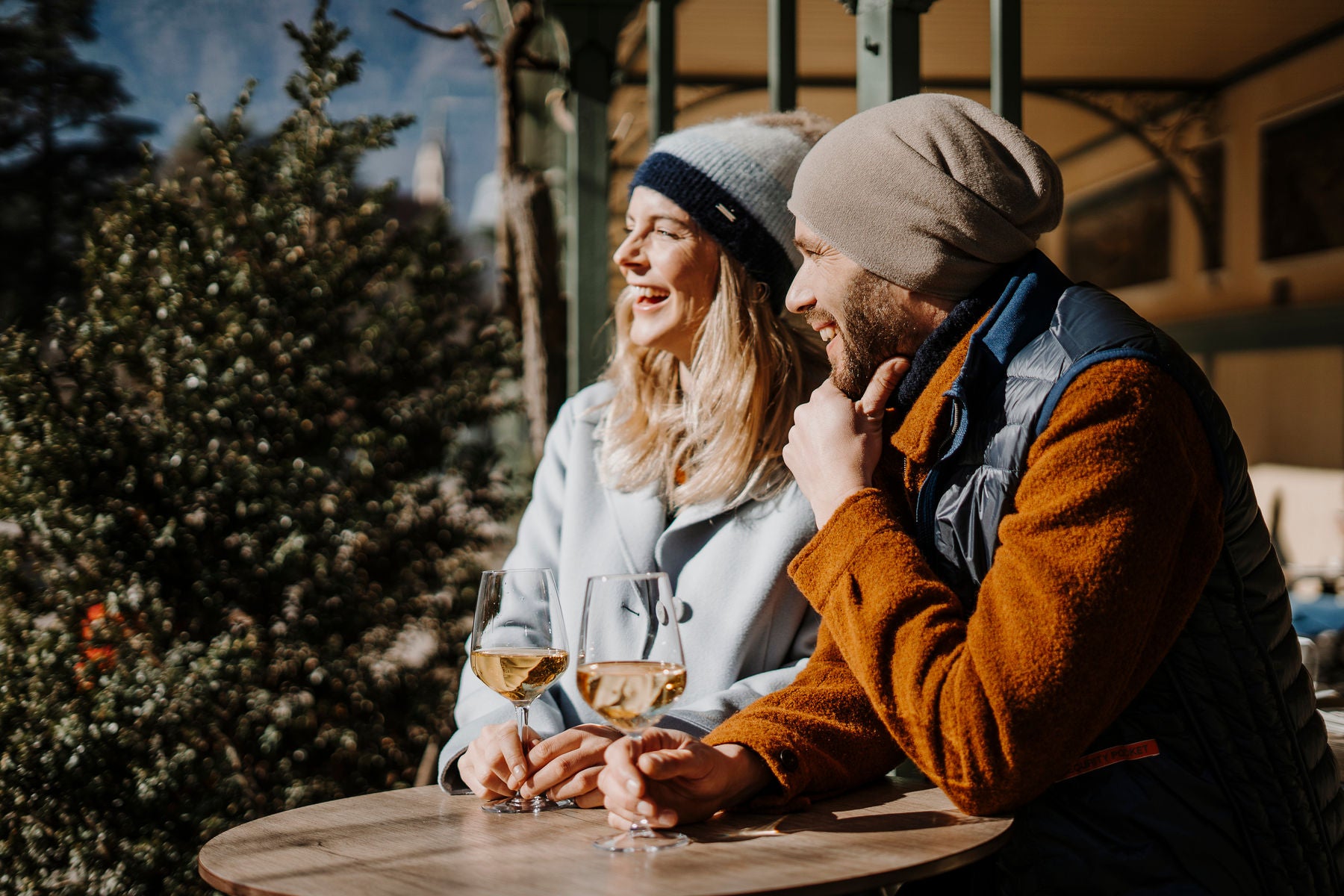 Eine Frau und ein Mann lächeln und trinken ein Glas Wein in der Kurstadt Meran.