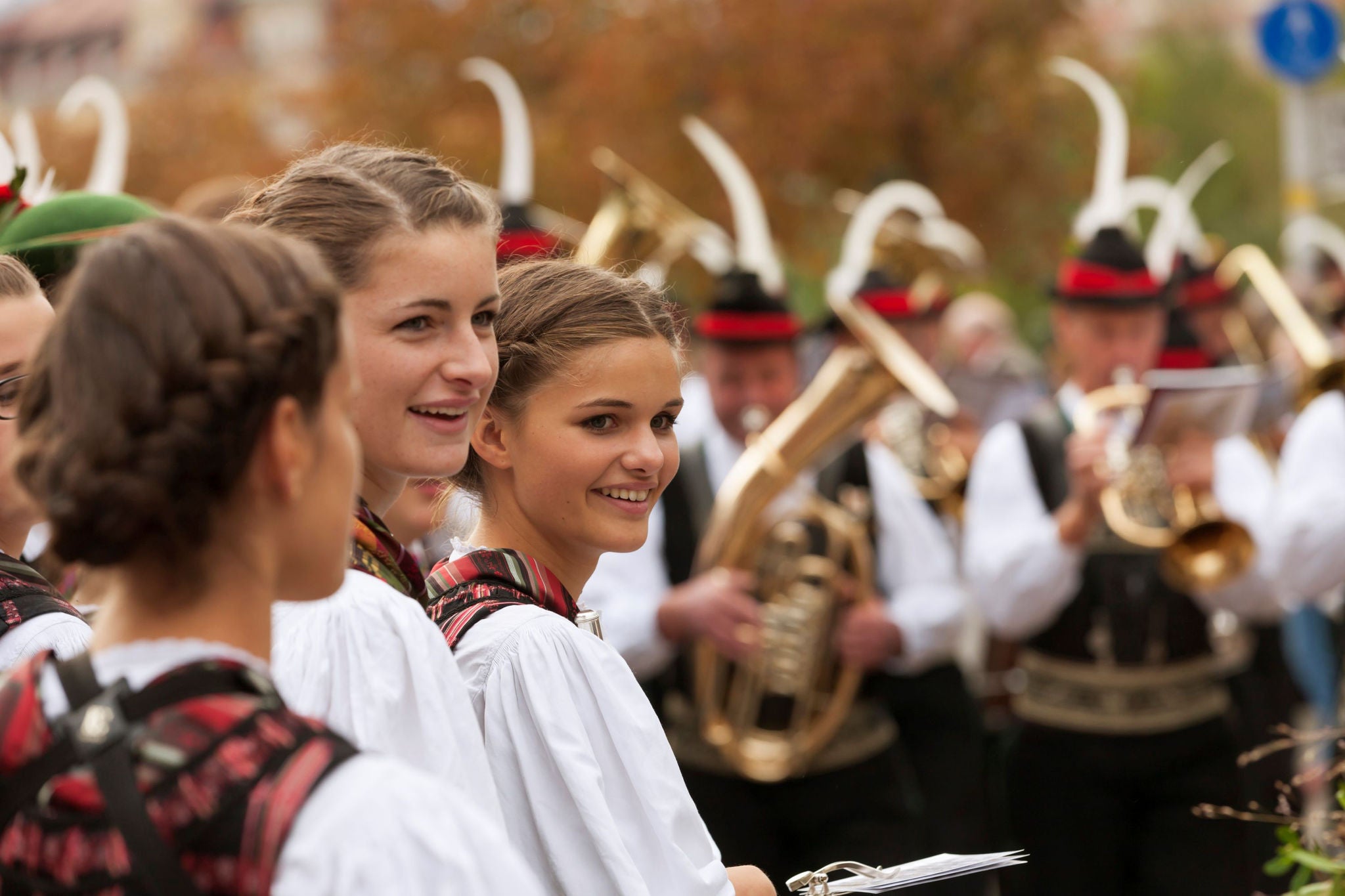 Junge Mädchen in der Tracht, dahinter spielt die Blaskapelle ebenfalls in typischer Tracht.