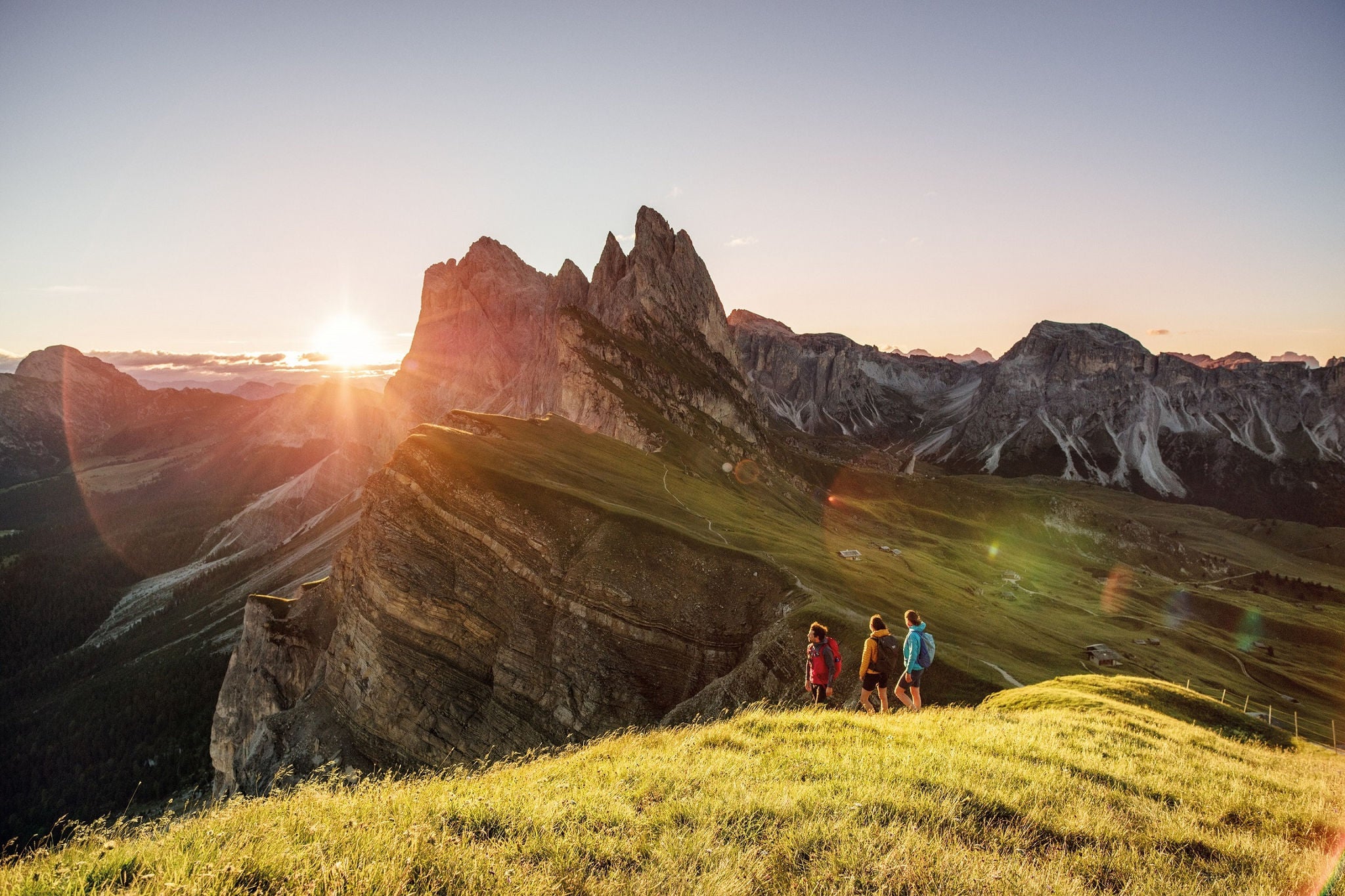 Drei Personen wandern mit dem Seceda im Hintegrund bei Sonnenuntergang