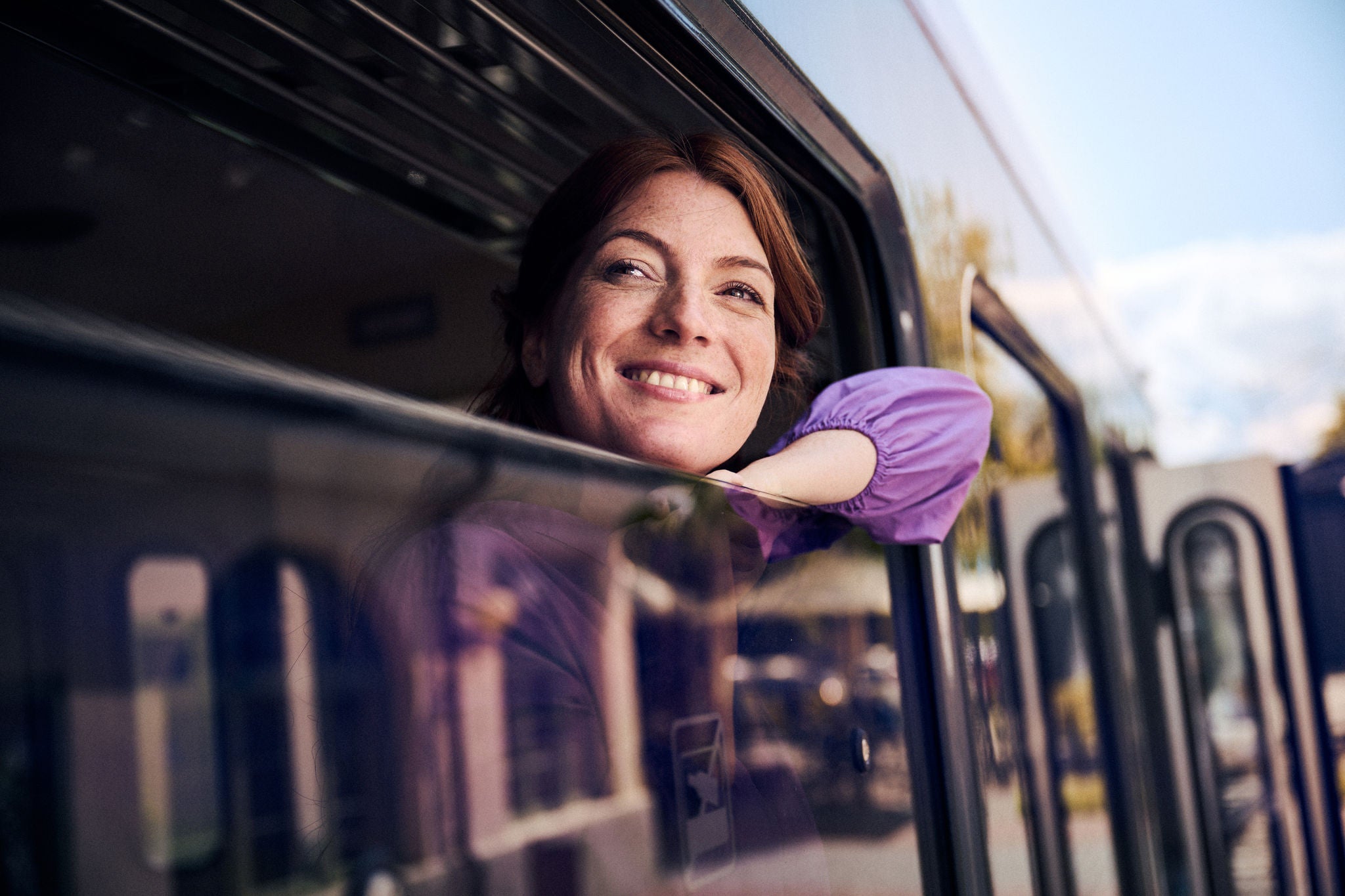 Dame mit lila Bluse bei Zugfahrt herauslehnend aus Zugfenster