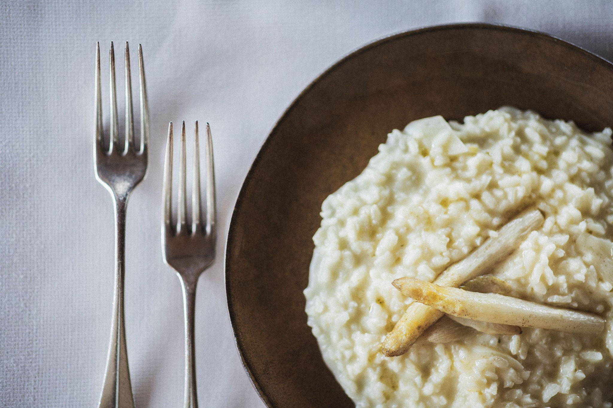 Ein Teller mit Risotto und weissen Spargeln, daneben zwei Gabeln.