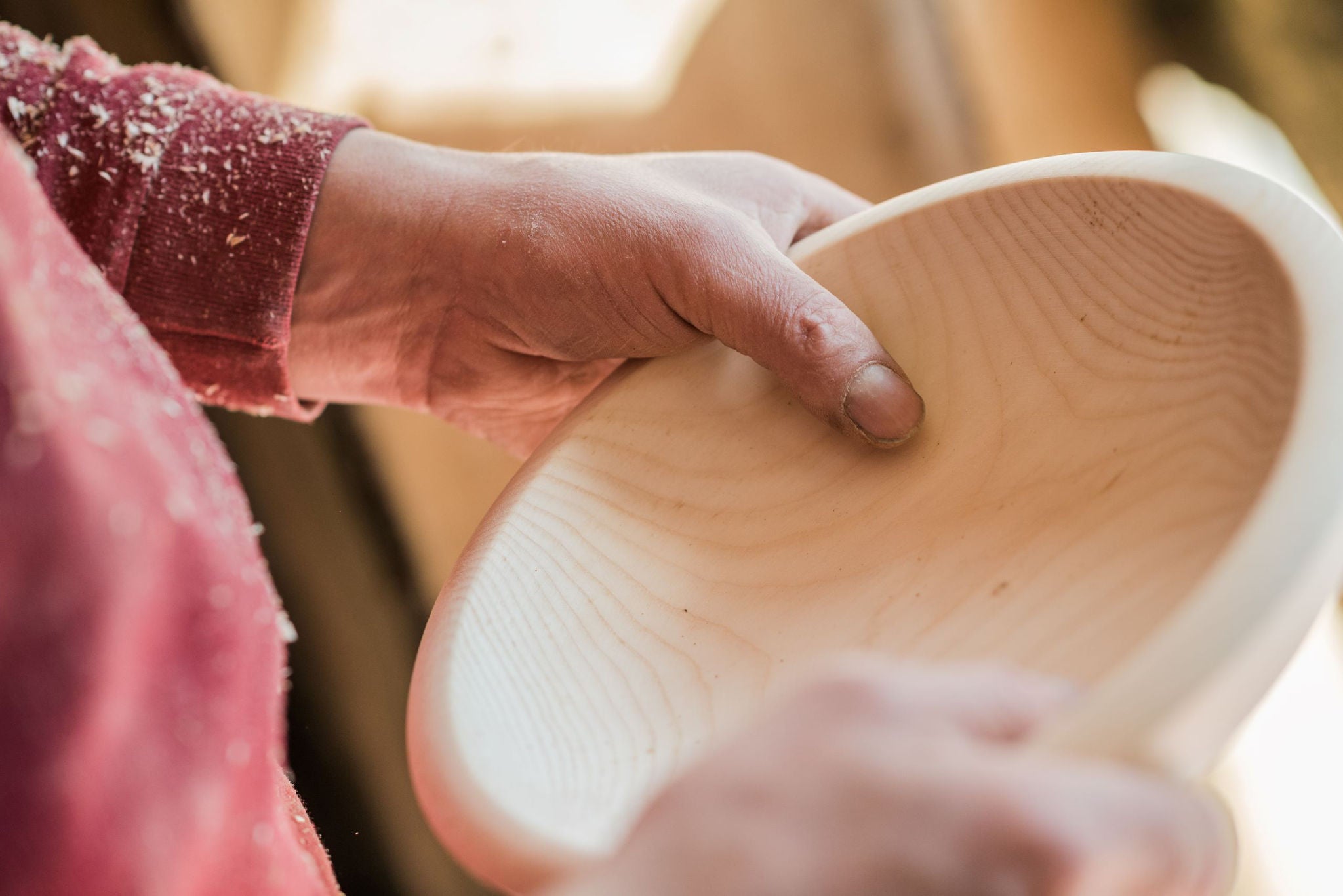 Zwei Hände eines Handwerkers halten eine fertig gedrechselte Schüssel aus Zirbenholz.