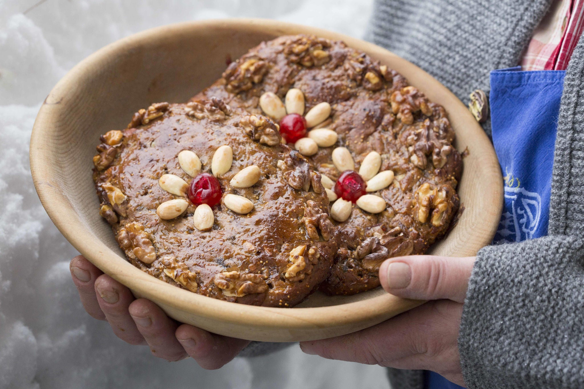 Eine Person hält eine Holzschale mit zwei Südtiroler Zelten, traditionellem Früchtebrot, das mit Mandeln verziert ist.