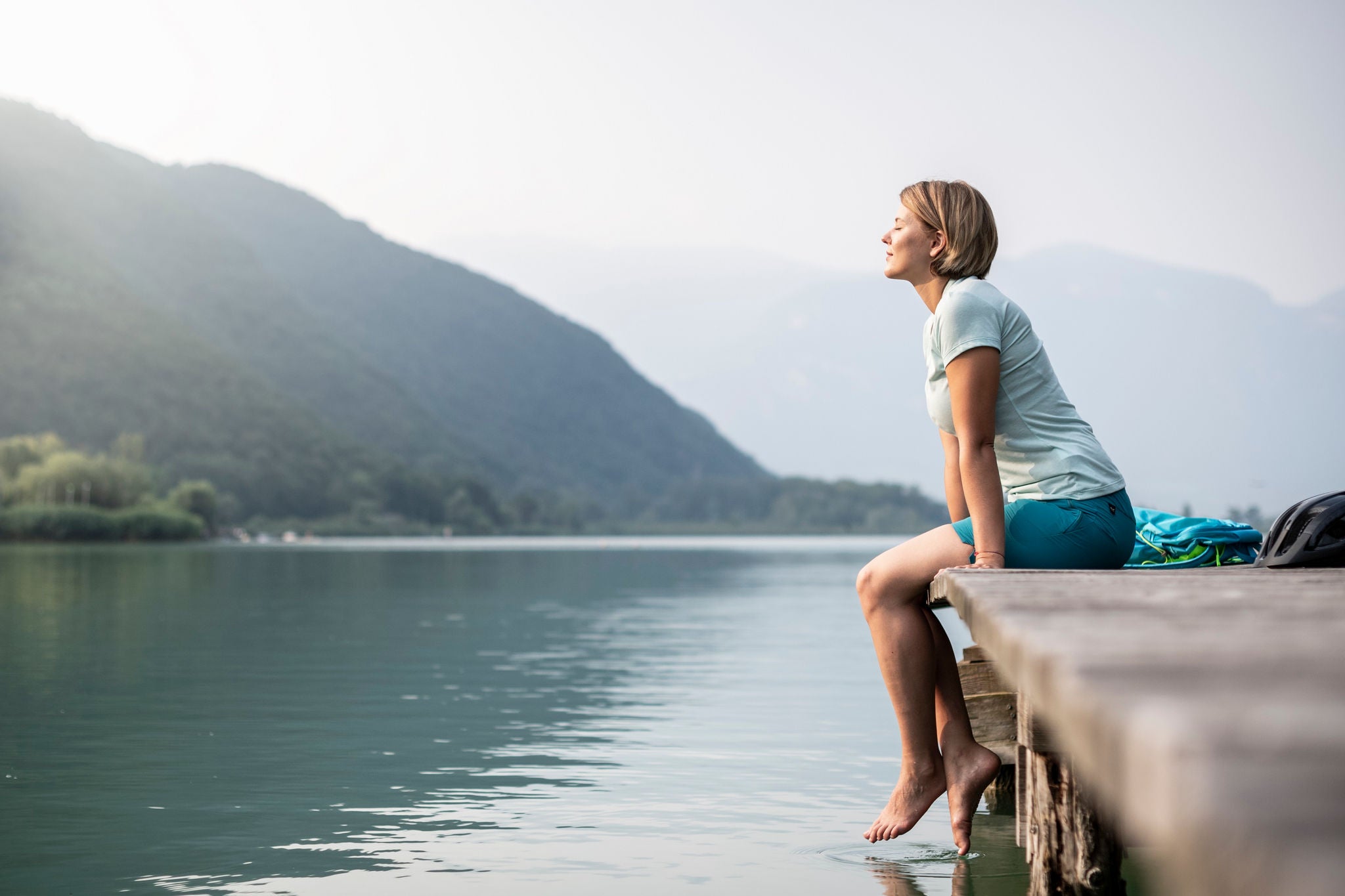 Eine Frau sitzt mit geschlossenen Augen auf einem Steg am Kalterer See.