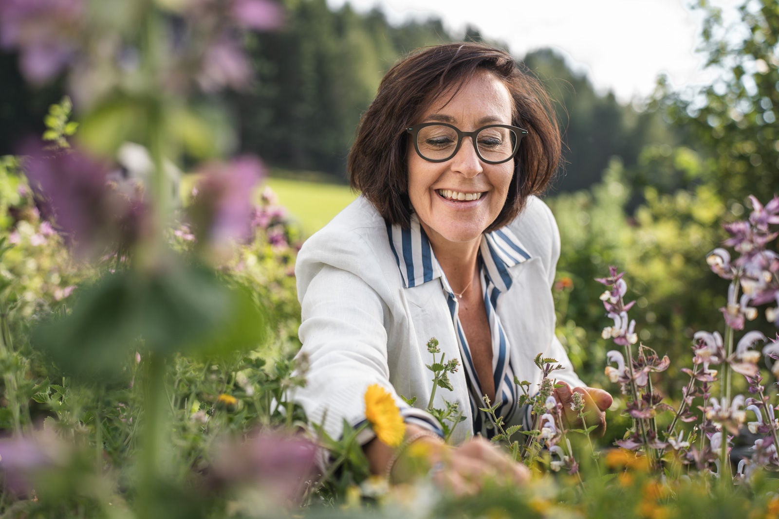 Gastwirtin Brigitte Zelger bückt sich lächelnd im hoteleigenen Kräutergarten zu blühenden Blumen hinunter.