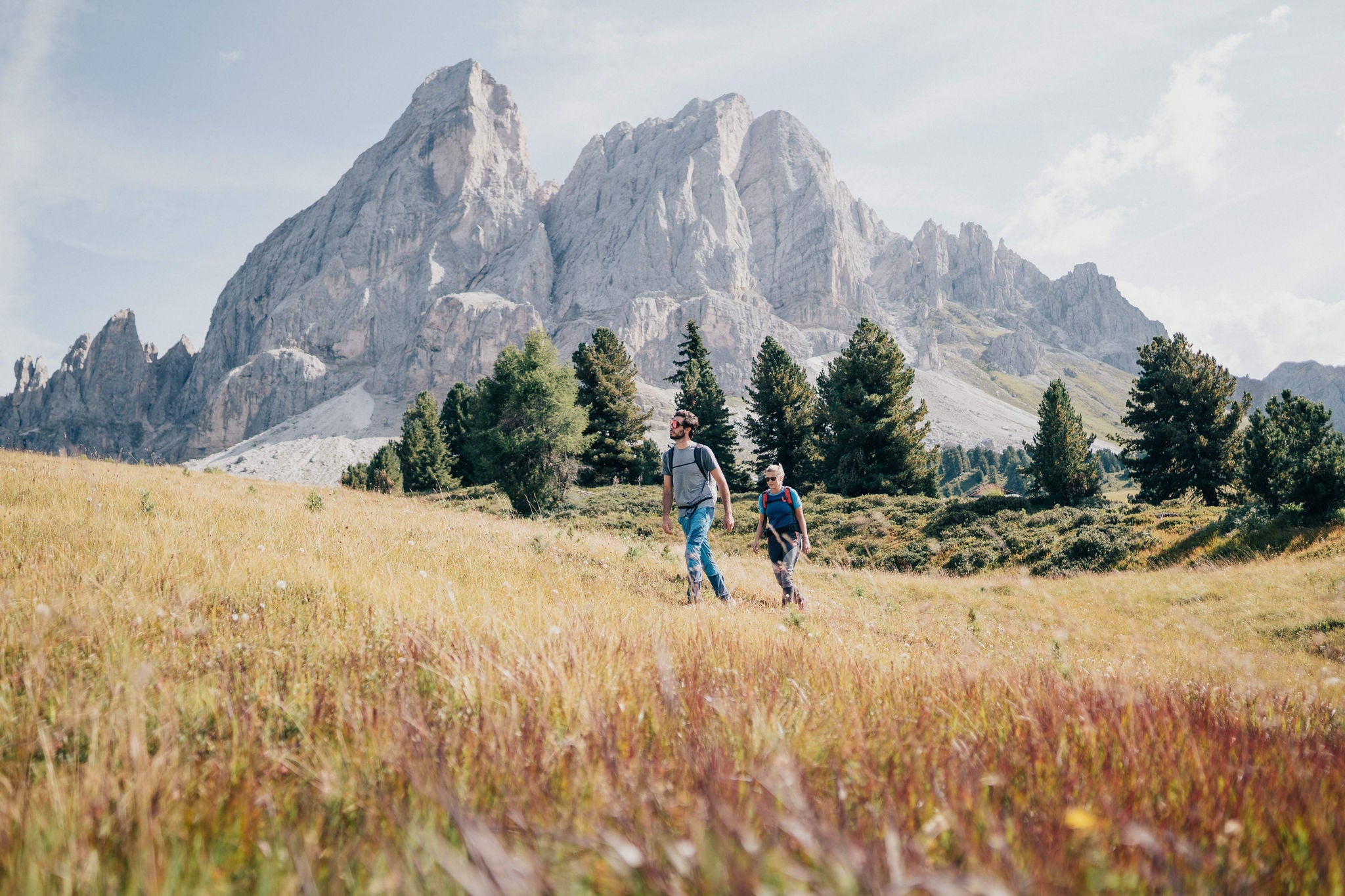 Eine Frau und ein Mann wandern über eine spätsommerliche Almwiese, im Hintergrund erhebt sich der Peitlerkofel.