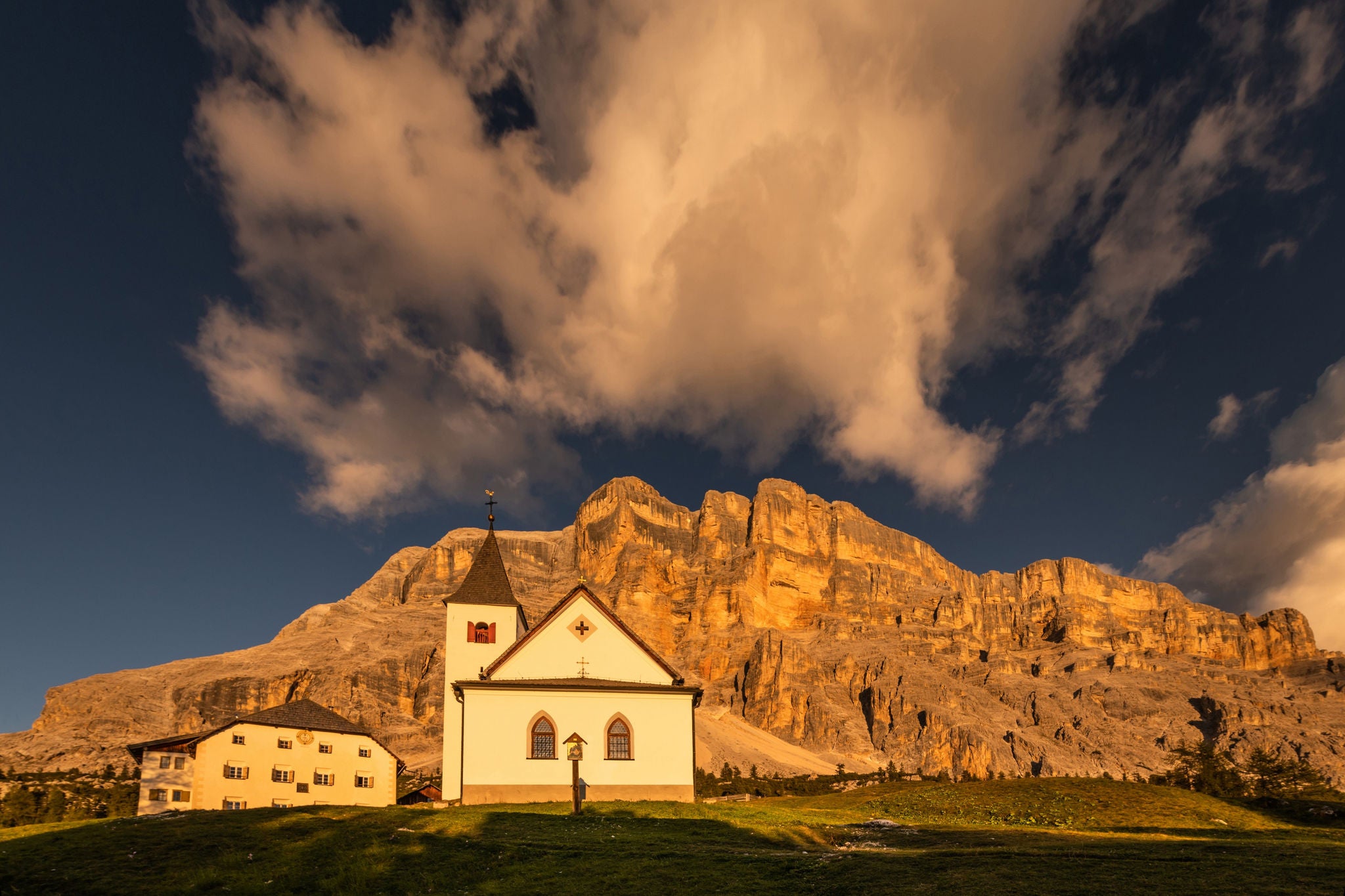 Eine kleine Kirche und ein Bauernhof vor dem vom Alpenglühen leuchtenden Bergmassiv Heiligkreuzkofel in Alta Badia