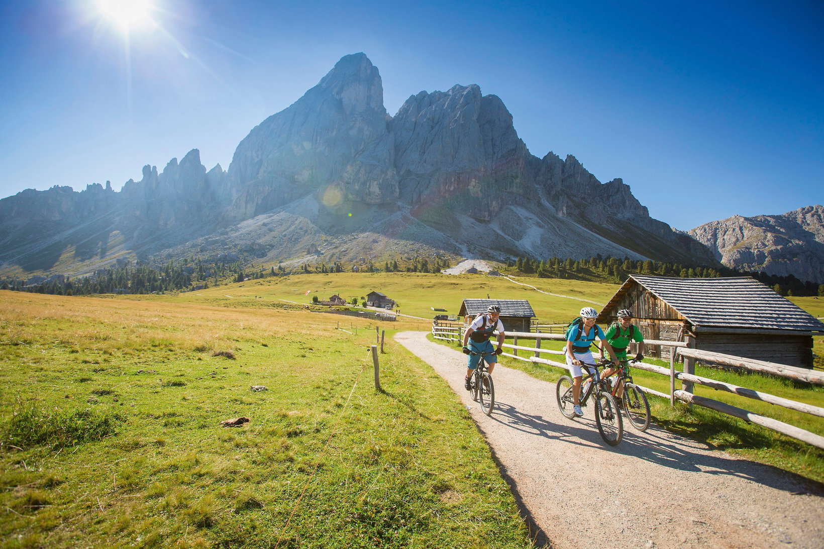 Drie mountainbikers genieten van een fietstocht bij de berg Peitlerkofel, die je op de achtergrond ziet.