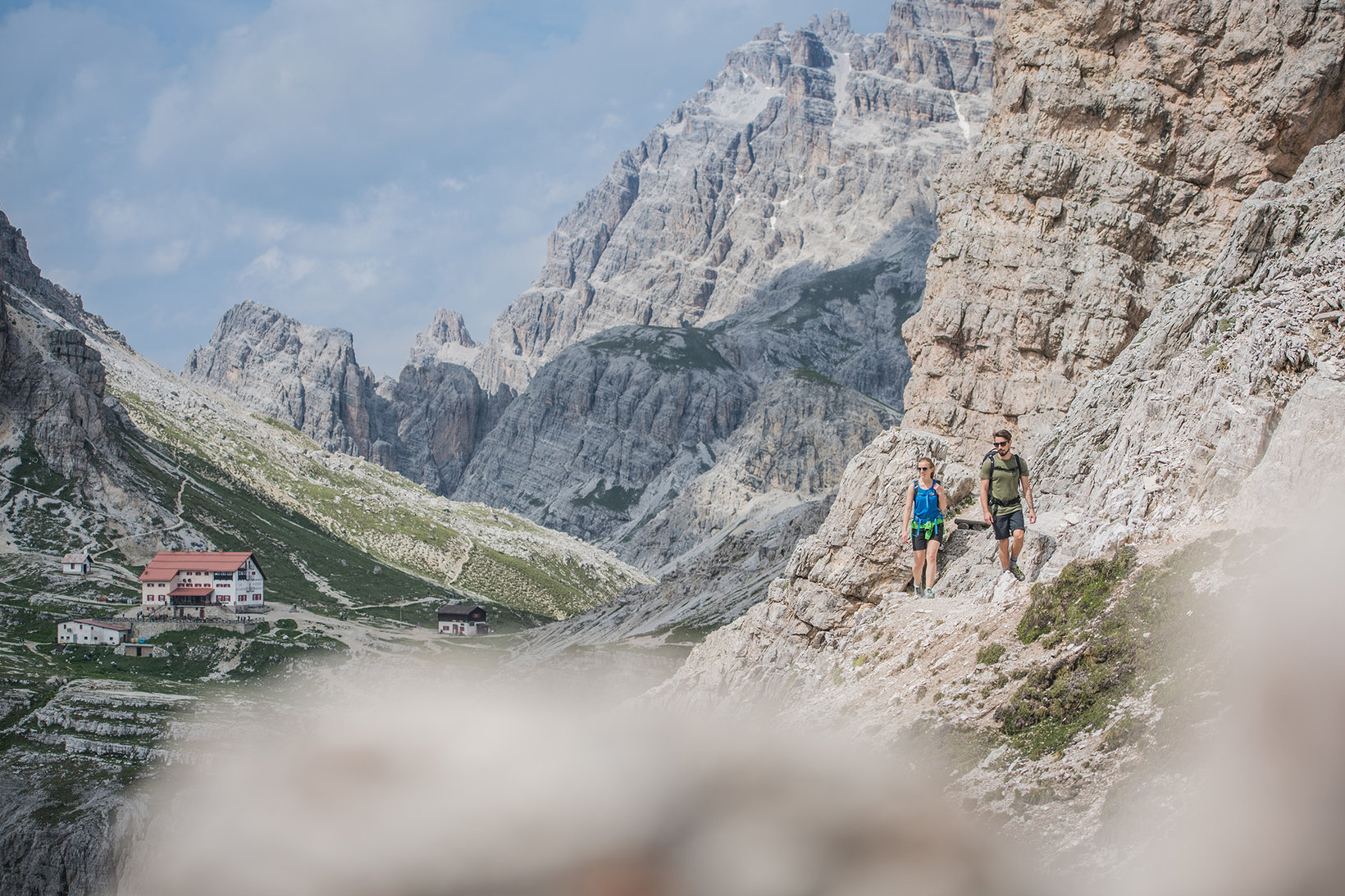 Ein Mann und eine Frau wandern durch die felsigen Dolomiten. Sie tragen kurze Wanderklamotten.