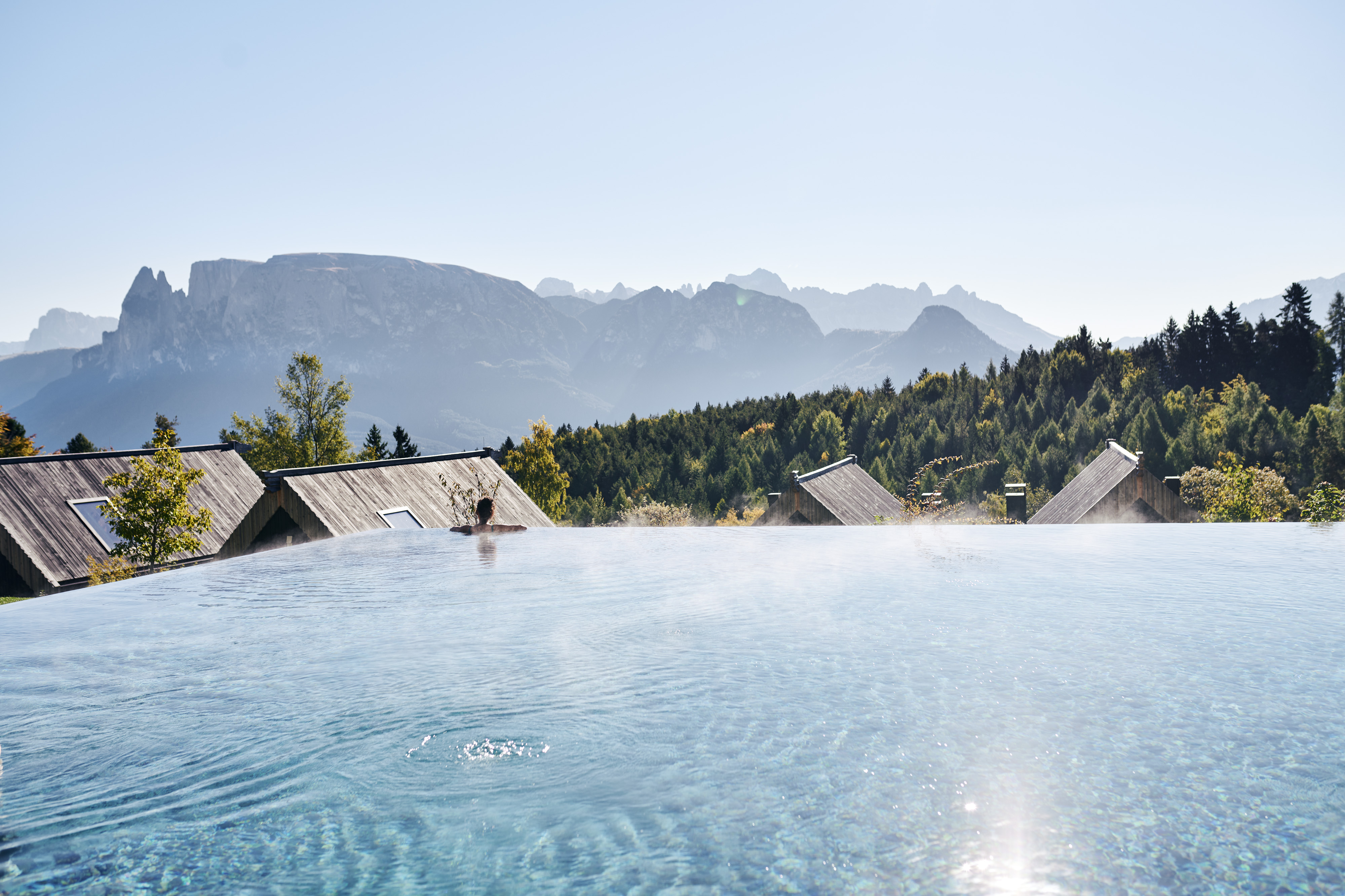 Una donna si rilassa in una piscina all'aperto e si gode la vista del paesaggio montano circostante.