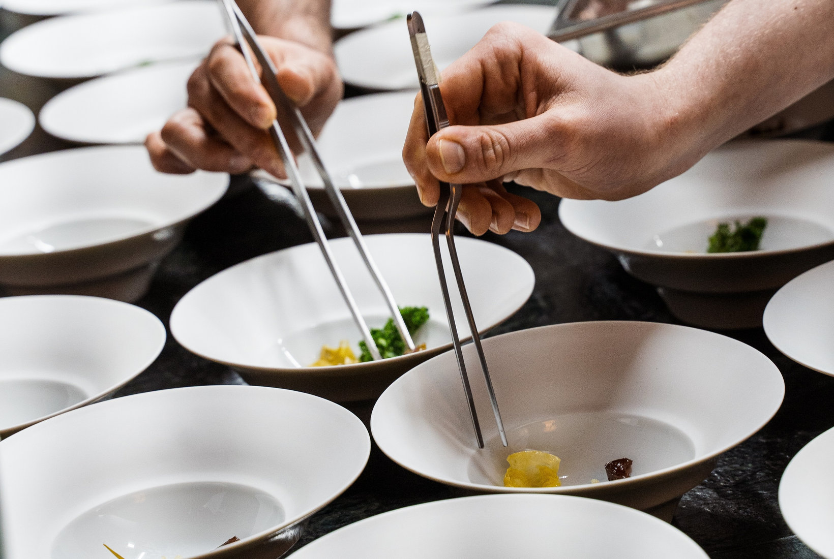 South Tyrolean red wine is poured into a glass next to a plate with a meat dish on an elegant white tablecloth.