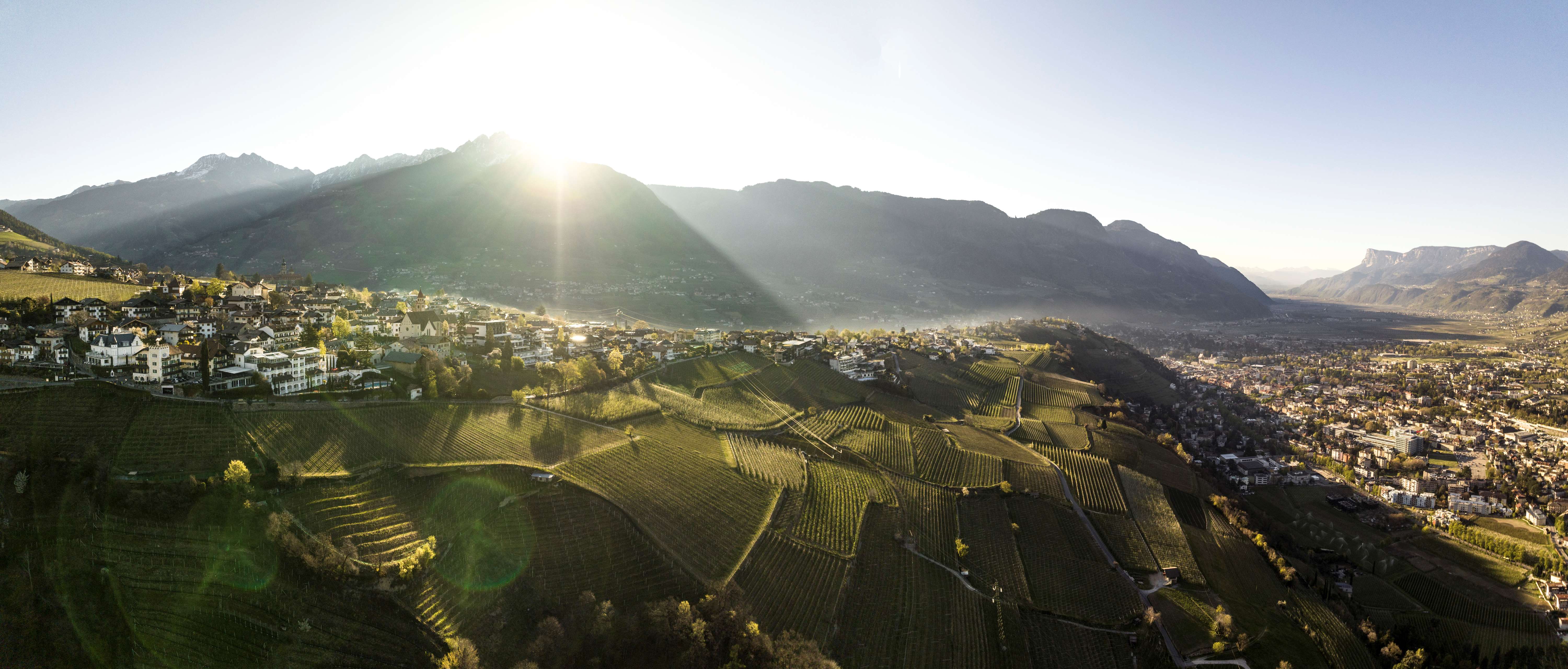 Výhled na Dorf Tirol v létě. Slunce svítí a vytváří světelné odrazy.