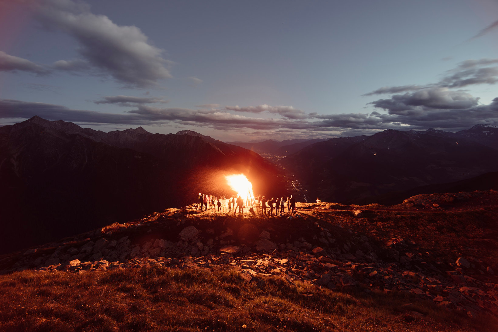 Looking towards Meran/Merano in the Passeiertal valley, locals gather around a traditional Sacred Heart bonfire on a June evening.